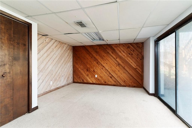 empty room with light carpet, wood walls, a drop ceiling, and visible vents