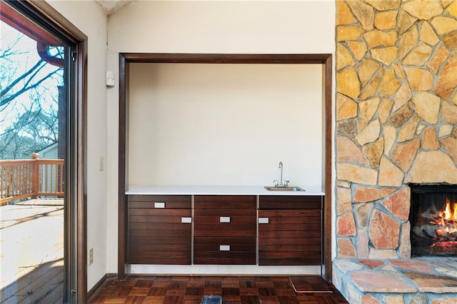 interior space featuring lofted ceiling, a stone fireplace, a sink, baseboards, and wet bar