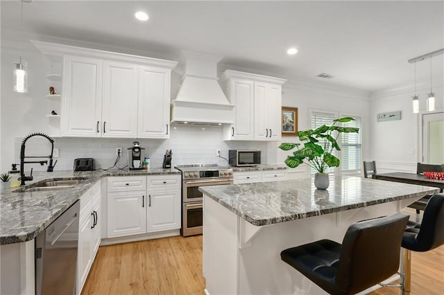 kitchen with decorative light fixtures, premium range hood, white cabinets, and stainless steel appliances