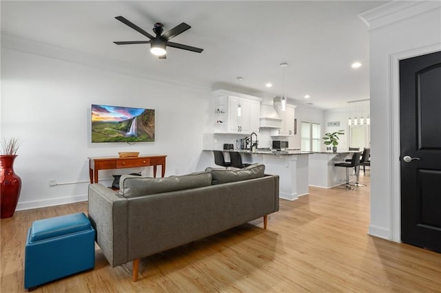 living room featuring light wood-type flooring, ceiling fan, and ornamental molding