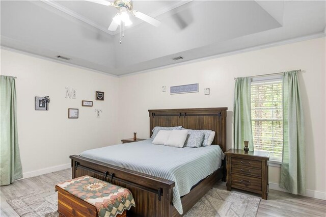 bedroom with visible vents, multiple windows, light wood-style flooring, ornamental molding, and a raised ceiling