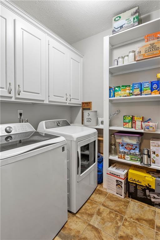 clothes washing area with washer and clothes dryer, cabinet space, and a textured ceiling