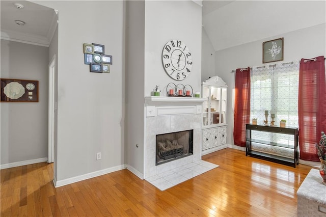 living room with a tiled fireplace, hardwood / wood-style floors, crown molding, baseboards, and vaulted ceiling