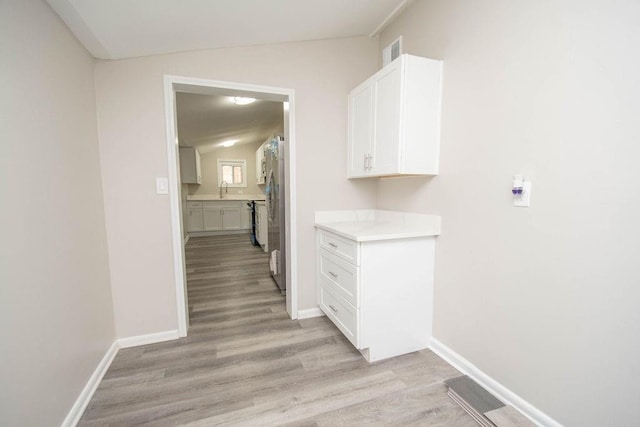 hallway featuring light wood-type flooring, baseboards, visible vents, and a sink