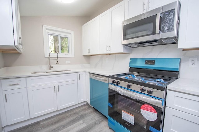 kitchen with light wood-style flooring, stainless steel appliances, a sink, light countertops, and white cabinets