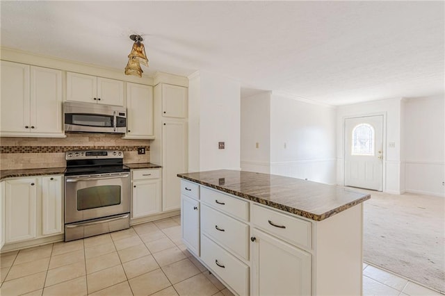 kitchen featuring dark stone countertops, backsplash, stainless steel appliances, a center island, and light carpet