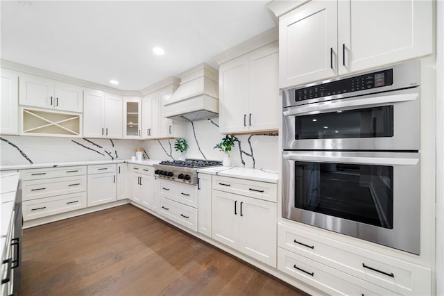 kitchen featuring dark wood-type flooring, stainless steel appliances, decorative backsplash, custom exhaust hood, and white cabinetry