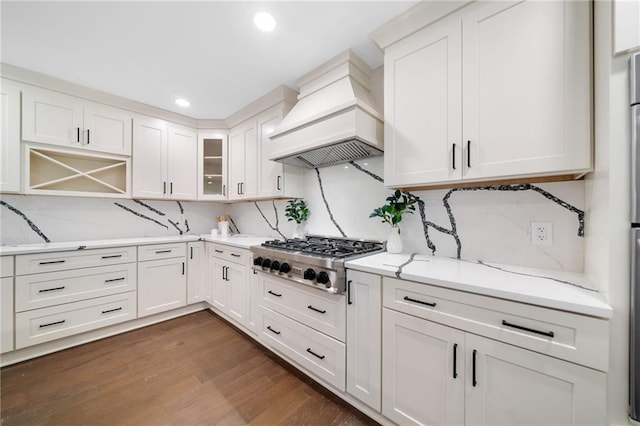 kitchen featuring dark wood-type flooring, stainless steel gas stovetop, premium range hood, light stone countertops, and white cabinetry