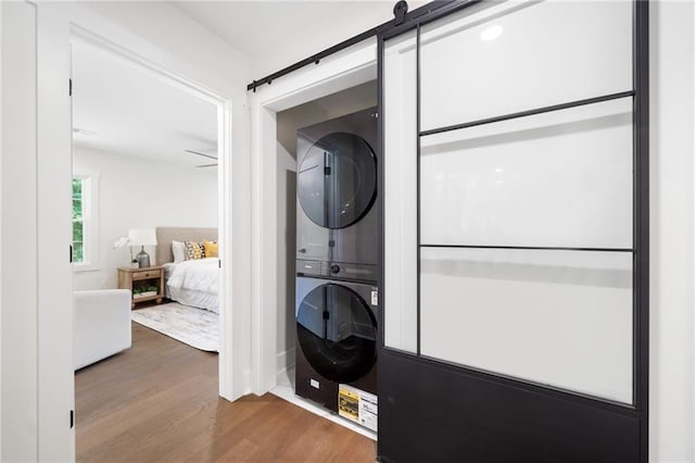 laundry area with ceiling fan, stacked washer / drying machine, a barn door, and wood-type flooring