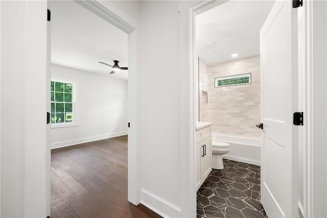 full bathroom featuring toilet, vanity, tiled shower / bath, hardwood / wood-style flooring, and ceiling fan