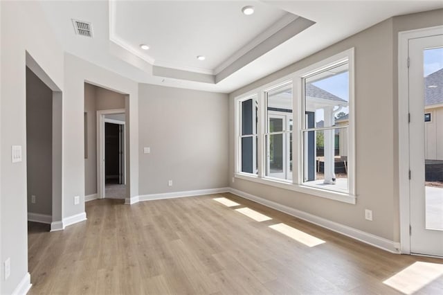 spare room featuring ornamental molding, visible vents, light wood-style flooring, a raised ceiling, and baseboards