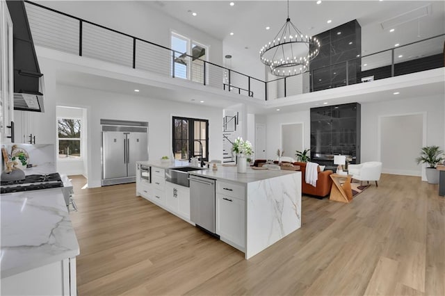 kitchen featuring white cabinetry, an island with sink, appliances with stainless steel finishes, a high ceiling, and light stone countertops