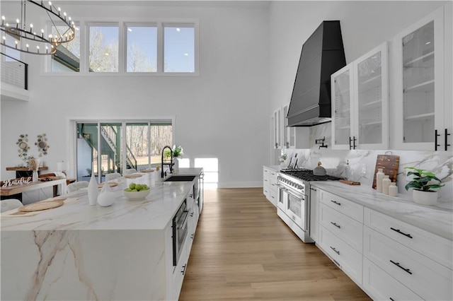 kitchen featuring pendant lighting, white cabinetry, stainless steel appliances, light stone counters, and custom range hood