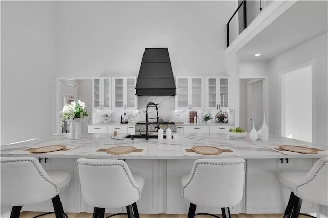 kitchen featuring a breakfast bar area, white cabinetry, and premium range hood