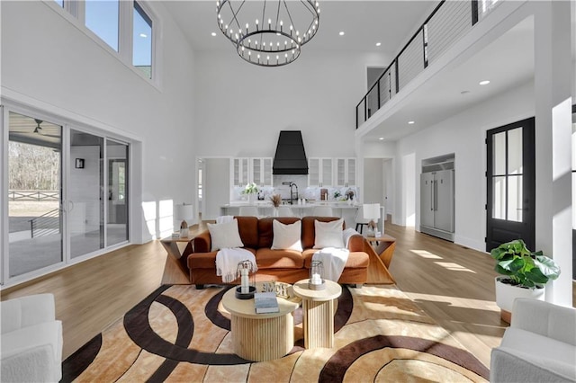 living room with light wood-type flooring, a chandelier, a towering ceiling, and sink