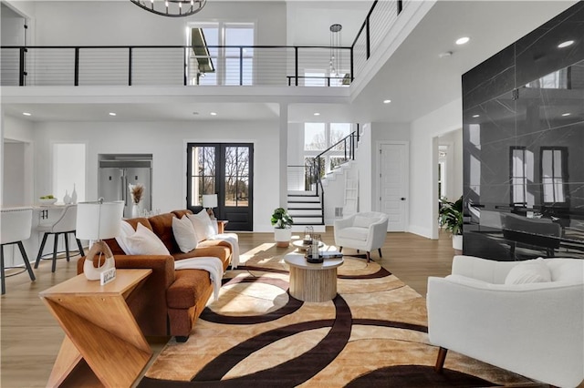 living room featuring a towering ceiling, light hardwood / wood-style flooring, french doors, and a notable chandelier