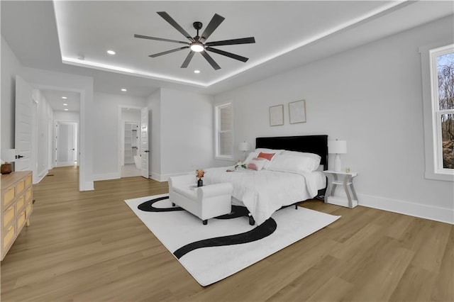 bedroom with ceiling fan, a raised ceiling, and light hardwood / wood-style floors