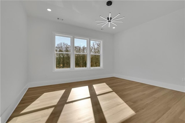 empty room with a notable chandelier and light hardwood / wood-style floors