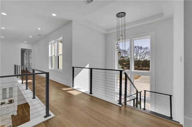 hallway featuring wood-type flooring, a raised ceiling, and a healthy amount of sunlight