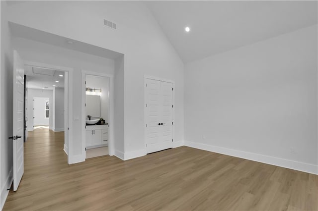 unfurnished bedroom featuring connected bathroom, light wood-type flooring, a closet, high vaulted ceiling, and sink