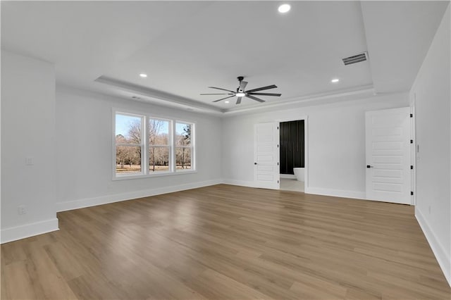 empty room with ceiling fan, light hardwood / wood-style flooring, and a raised ceiling