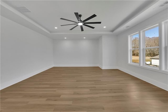 empty room featuring ceiling fan, a tray ceiling, and light hardwood / wood-style flooring