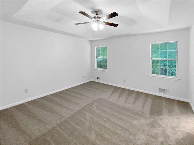 empty room with carpet floors, a raised ceiling, and ceiling fan