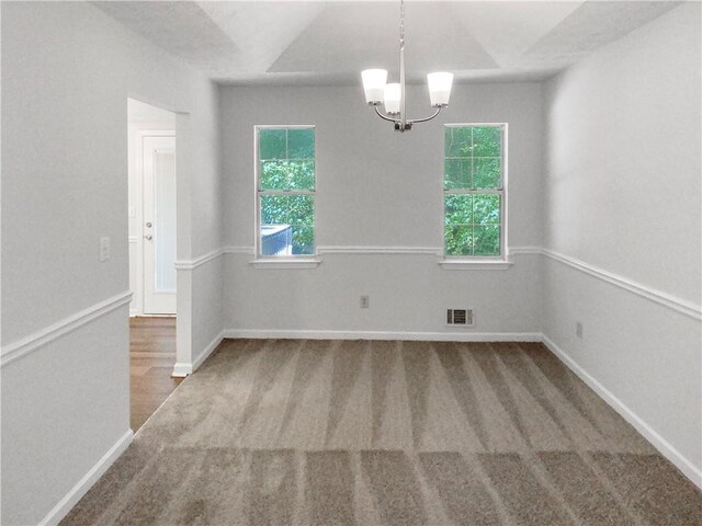 spare room featuring an inviting chandelier, dark colored carpet, and plenty of natural light