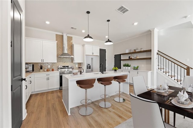 kitchen with a kitchen island with sink, electric stove, wall chimney range hood, decorative light fixtures, and white cabinetry