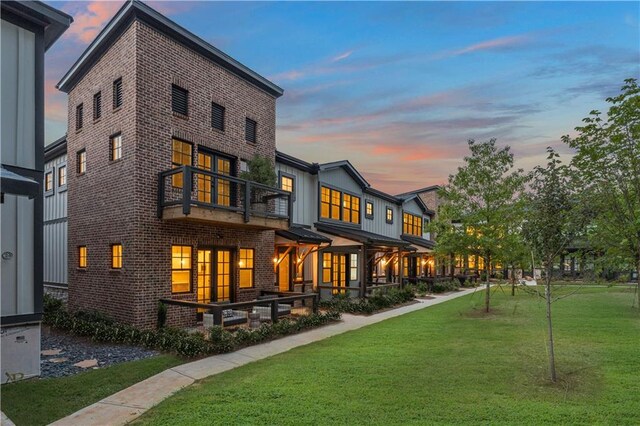 back house at dusk with a yard and a balcony