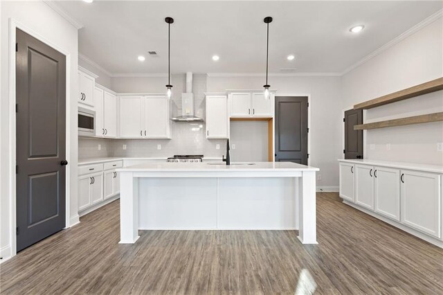 kitchen featuring appliances with stainless steel finishes, wall chimney exhaust hood, pendant lighting, a center island with sink, and hardwood / wood-style floors