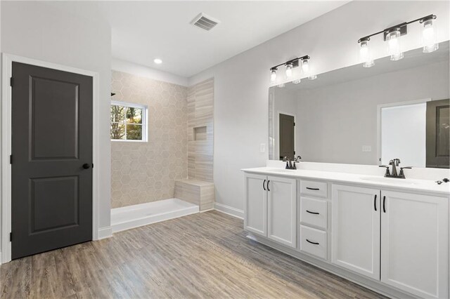 bathroom with hardwood / wood-style floors, vanity, and a tile shower