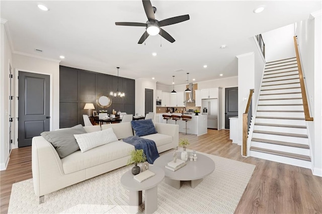 living room with light wood-type flooring, ceiling fan with notable chandelier, and ornamental molding