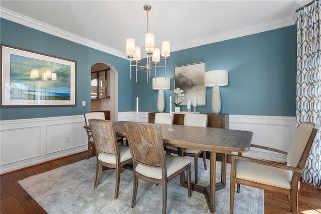 dining space with arched walkways, a wainscoted wall, wood finished floors, crown molding, and a notable chandelier