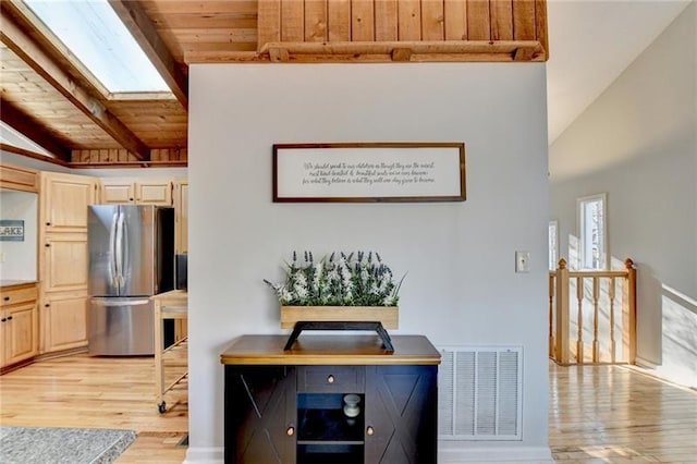 kitchen with freestanding refrigerator, a skylight, light wood-type flooring, wooden ceiling, and light brown cabinets