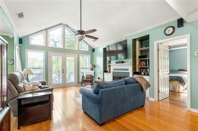 living room with built in shelves, ceiling fan, ornamental molding, french doors, and light hardwood / wood-style flooring