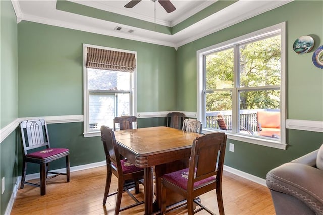 dining area with ceiling fan, light wood-type flooring, ornamental molding, and a tray ceiling