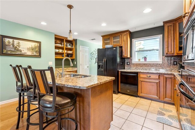 kitchen with a kitchen island with sink, pendant lighting, sink, decorative backsplash, and black appliances