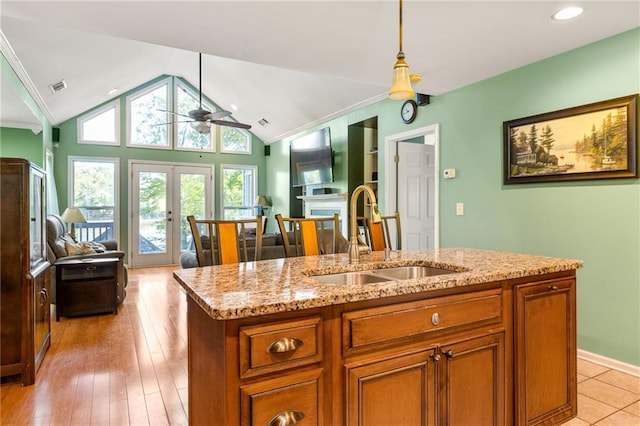 kitchen with light hardwood / wood-style floors, vaulted ceiling, sink, french doors, and an island with sink