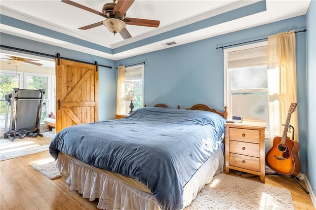 bedroom with a barn door, a raised ceiling, light hardwood / wood-style flooring, and ceiling fan