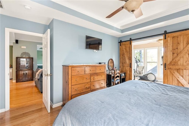 bedroom featuring ceiling fan, a barn door, ornamental molding, and wood-type flooring