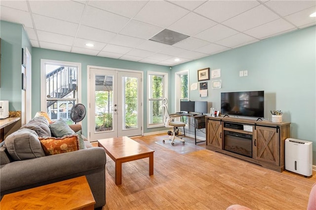 living room with a drop ceiling, light wood-type flooring, and french doors