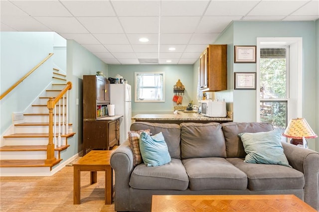 living room featuring light wood-type flooring and a paneled ceiling