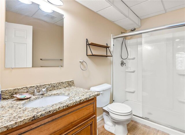 bathroom featuring a drop ceiling, toilet, hardwood / wood-style floors, a shower with shower door, and vanity