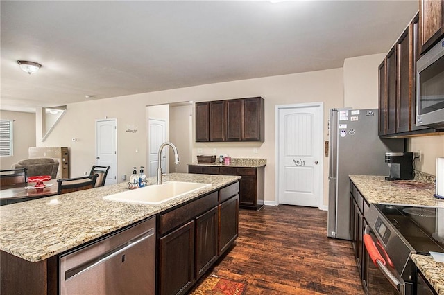 kitchen with dark brown cabinets, a sink, dark wood-type flooring, stainless steel appliances, and an island with sink