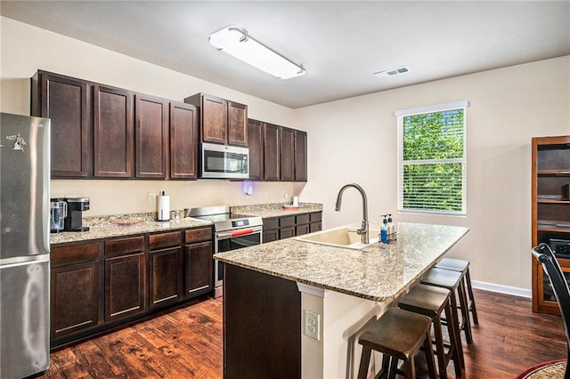 kitchen featuring appliances with stainless steel finishes, a sink, a breakfast bar area, visible vents, and dark wood-style floors