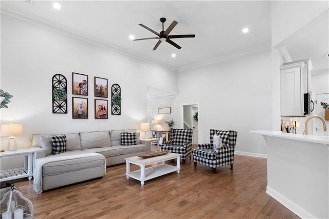 living room with light wood finished floors, baseboards, ornamental molding, recessed lighting, and a ceiling fan