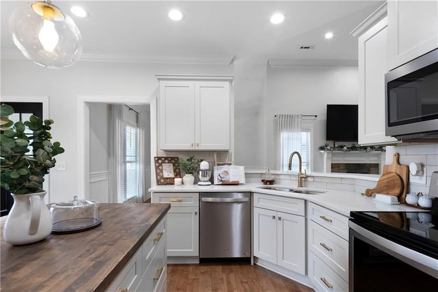 kitchen featuring ornamental molding, wooden counters, appliances with stainless steel finishes, and a sink