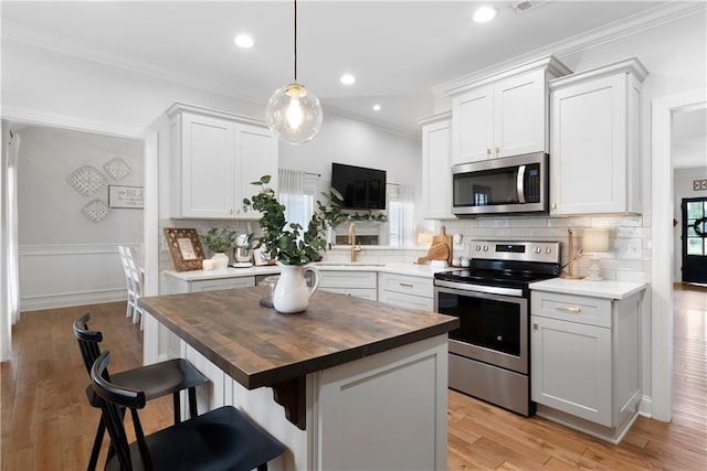 kitchen with a breakfast bar area, wooden counters, a sink, stainless steel appliances, and crown molding