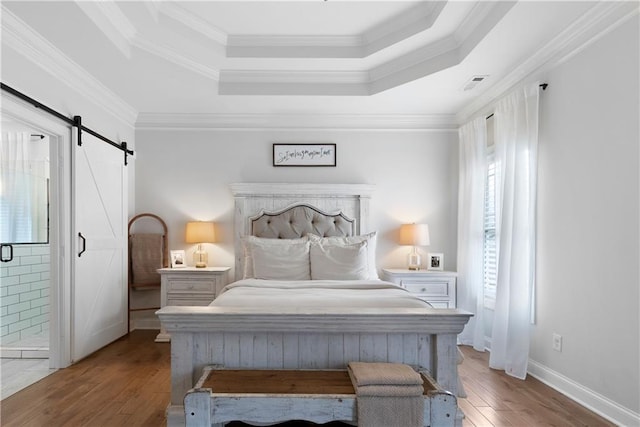 bedroom featuring a tray ceiling, a barn door, visible vents, and wood finished floors